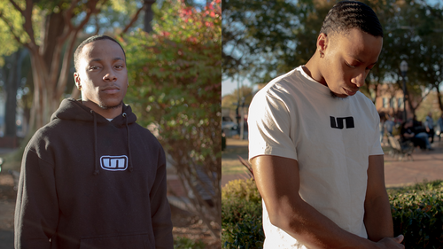 A model wearing the UNLONELY Box Logo Hoodie in the Black colorway and the UNLONELY Logo Tee in the Cream colorway.